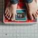 From above crop anonymous barefoot child in jeans standing on weigh scales on tiled floor of bathroom